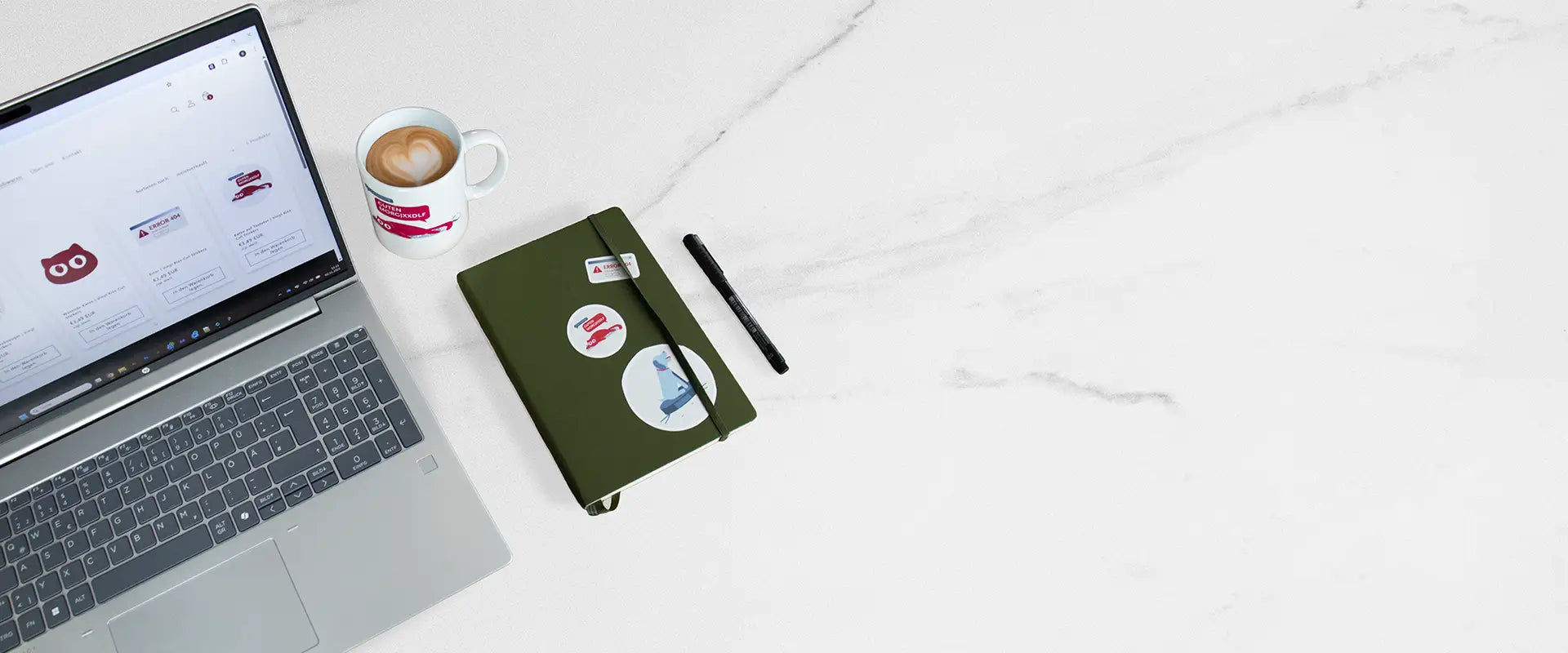 Ein Büro Schreibtisch, auf dem ein Laptop, eine Kaffeetasse und ein Notebook steht. Alles ist verschönert mit Produkten von Bugs and Mugs. 